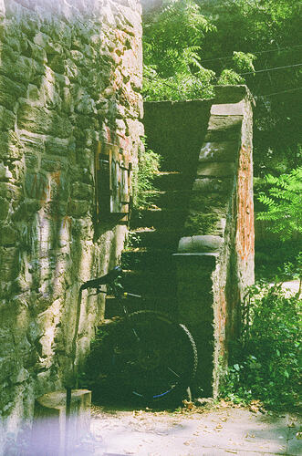 color film photo of my unicycle leaning against some stairs on the outside of a cobblestone structure