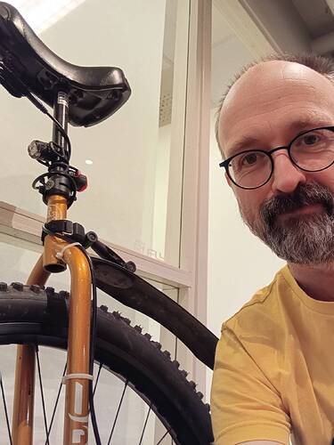 Man smiling into the camera next to a unicycle with a golden brown frame. The uni has a winter tyre, lights and a mudguard