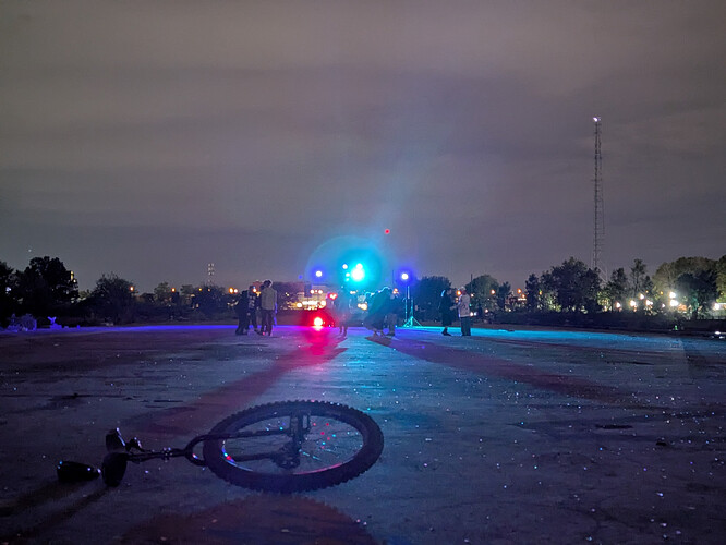photo of my unicycle laying on the concrete ground in front of a small rave setup with colorful lights shining towards the camera