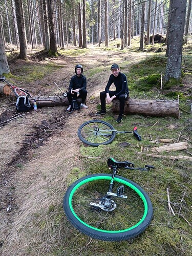 Two people reasting in a wooded area with unicycles in front of them