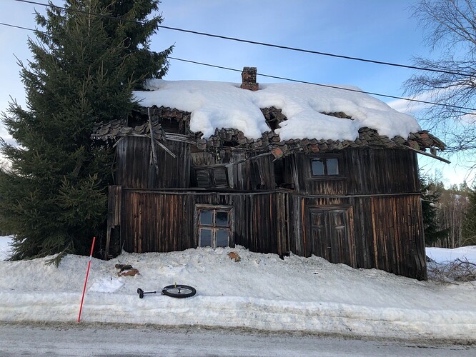 Old damaged cabin with the roof and top floor caving in, with unicycle lying in front